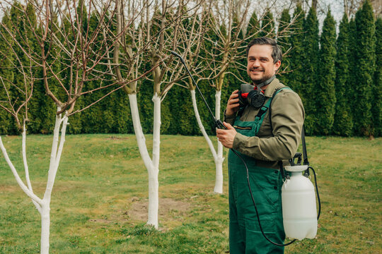 Gardener smiling with pesticide sprayer in spring orchard
