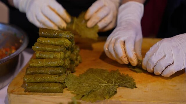 Close-up of a team preparing stuffed grape leaves with olive oil, showcasing traditional Turkish cuisine, teamwork in the kitchen, and handmade food preparation with fresh ingredients.