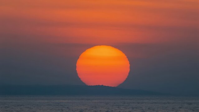 A sunset over the sea, with orange-red sky and mirror-like water reflections, creating a serene and healing travel atmosphere, making it a visual material image suitable for landscape and travel scena