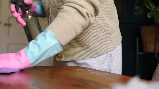 Woman in gloves wiping wooden table with cloth and spray bottle, slow dolly shot