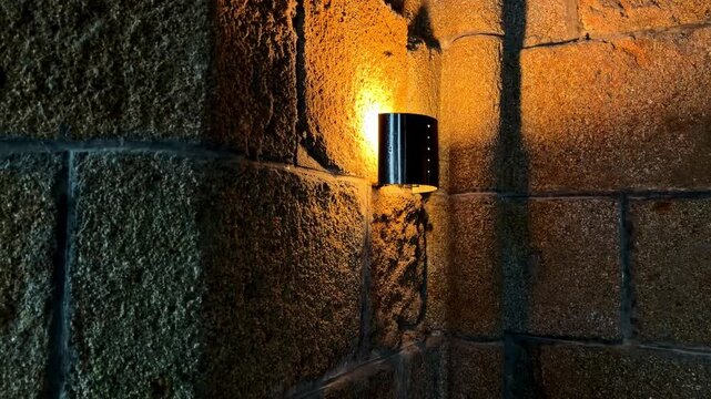 A warm light fixture casts a glow over the textured stone walls of a historic abbey. Ideal for historical documentaries or architectural studies.