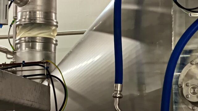 Blue hoses hang alongside stainless steel ducts in a factory environment. Useful for illustrating industrial processes or facility equipment layouts.