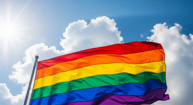 Waving rainbow flag against a blue sky with white clouds and sun flares, symbolizing pride, diversity, and equality for LGBTQ+ community