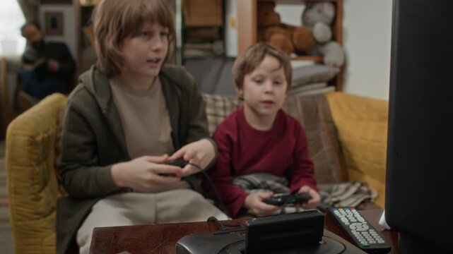 Boy inserting black game cartridge into classic console, while his younger brother eagerly awaiting start of game