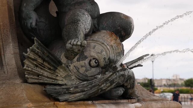Close up of a detail on a fountain in the city with water splashing from the mouth of a stone fish.