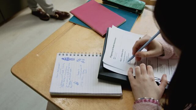 Over-shoulder close-up of female high school student writing multiple choice test on pregnancy during reproductive health lesson, reading questions and circling correct answers