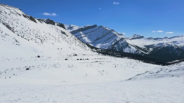 Banff, Canada ski mountains tower above evergreen forest, showcasing snowy Canadian Rockies terrain, rugged alpine ridges, and bright winter resort scenery.