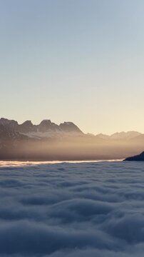 Low clouds blanket valley beneath snow-dusted mountains at sunrise near Walensee, Switzerland