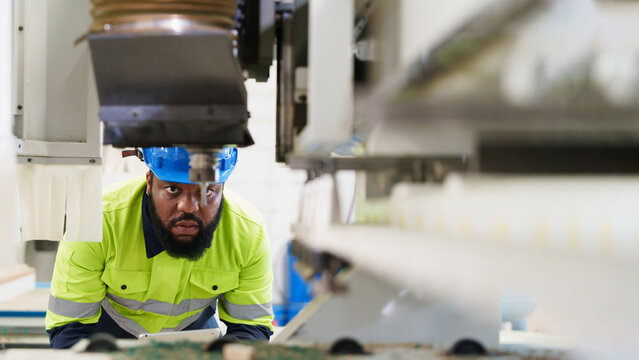 Worker in yellow high-visibility shirt and blue hard hat operates concrete CNC machine within gray concrete factory setting, focused on precision engineering and industrial maintenance.