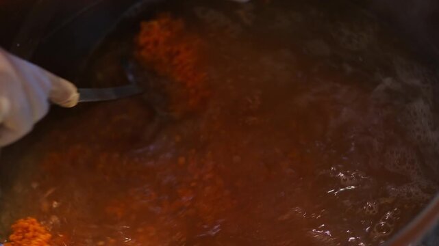 Ingredients simmer in a boiling pot as a rich soup mixture is stirred. The scene highlights the cooking process, bubbling texture, and careful preparation in a professional kitchen environment.