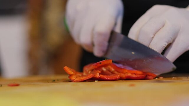 A red pepper is carefully sliced on a cutting board using a sharp knife. The process highlights fresh ingredient preparation, precision cutting, and detailed kitchen work in a culinary setting.