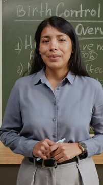 Medium vertical portrait of smiling female teacher explaining birth control methods for responsible pregnancy planning during sexual education lesson at high school, looking at camera