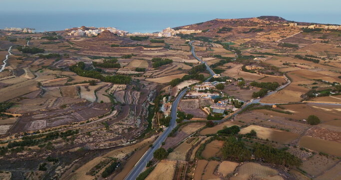 Malta, Comino island: rural landscape, showcasing cultivated fields, roads, and coastal town with buildings and blue ocean in the distance. Natural scene background. Aerial view drone flight