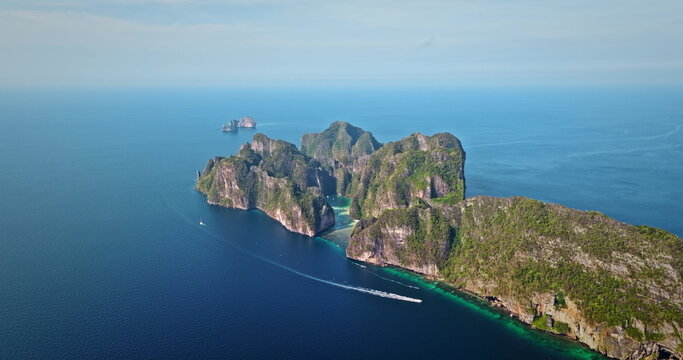 Tropical Phi Phi island displaying lush green limestone cliffs rising from turquoise water with boat cruising past, offering a stunning travel destination and vacation landscape. Aerial drone panorama
