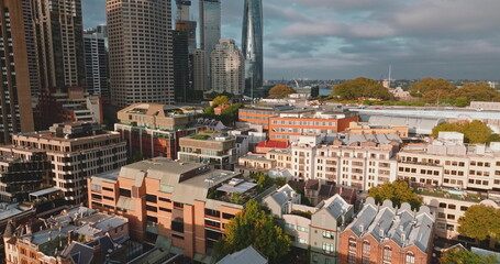 Naklejka premium Australia, Sydney City: modern downtown skyscrapers and historic low-rises buildings houses under bright cloudy sky, highlighting urban development. Drone flight aerial view