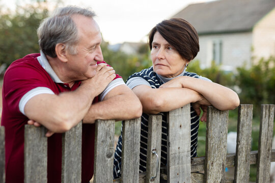 Happy married elderly couple have conversation near the fence of their farm