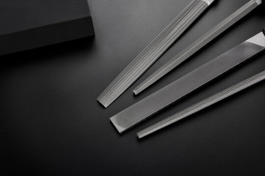 Assorted metal files for craft and industrial work including flat and round profiles, professional hand tools for shaping metal and wood on a dark surface.