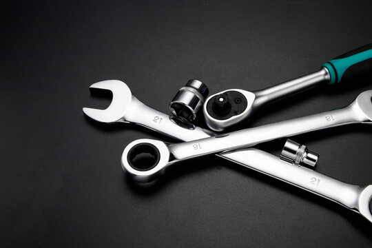 Professional chrome vanadium steel hand tools including ratchet wrench sockets and combination spanners set on a dark black background for automotive repair and maintenance work