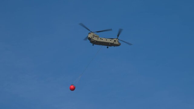 Transport helicopter of Dutch Royal Air Force carrying a water bucket for extinguishing wildfires in nature.