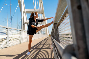Sporty woman in headphones doing stretching exercise on the urban bridge during outdoor workout. © Barillo Images