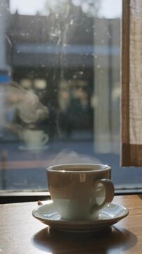 Warm morning light streams through a cafe window as steam rises from a coffee cup, creating a calm cinematic scene ideal for lifestyle marketing, relaxation apps, or cozy branding visuals