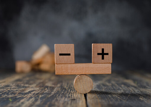 Plus and minus balance concept. Positive and negative symbols on wooden blocks are in balance on a wooden seesaw. Copy space