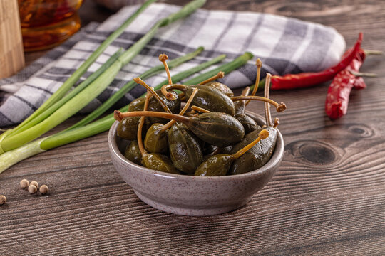 Pickled caper berries in a bowl with fresh ingredients on a rustic wooden table.