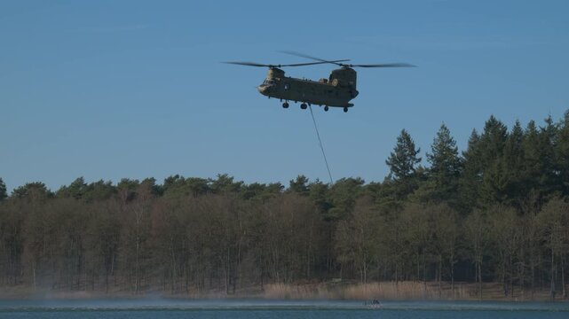 Transport helicopter of Dutch Royal Air Force carrying a water bucket for extinguishing wildfires in nature.