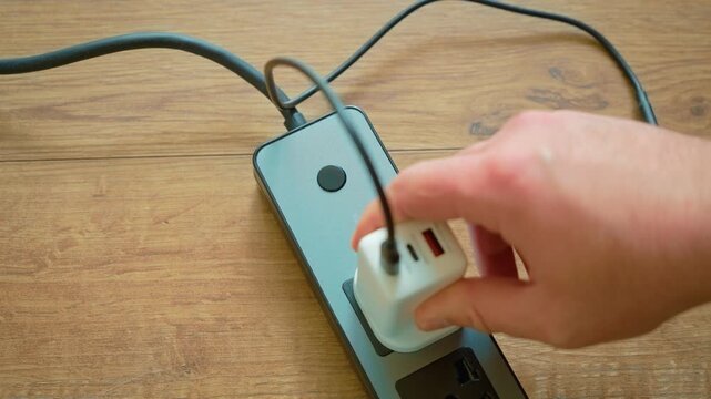 Plugging USB wall charger with Type G UK plug into portable power strip socket. Hand inserting charging adapter with British standard plug connecting to extension outlet for energy supply. Power
