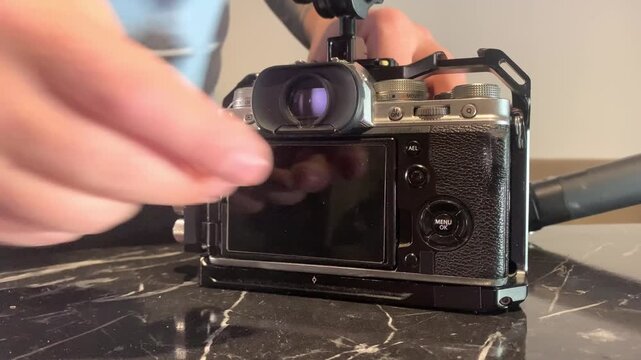 Hands rotating camera monitor on cage close-up, adjusting screen angle for better viewing and framing, optimizing shooting workflow and control during video production and filming setup