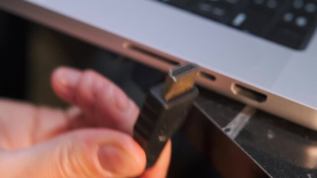 hand removing hdmi cable close-up shot from laptop port, device disconnection process showing video signal interruption and hardware unplugging in modern workspace environment
