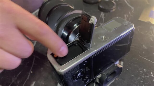 Hands inserting battery into camera compartment close-up, placing power cell into slot, securing it inside mirrorless body, demonstrating essential preparation step for photography and video shooting