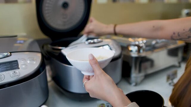 Woman Scooping Steamed Rice Into White Bowl at Buffet Station