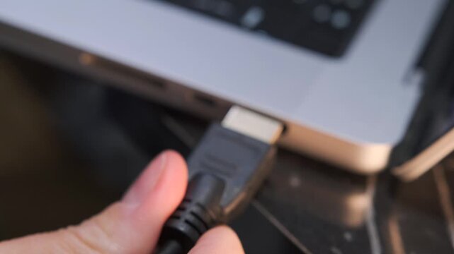 hand inserting hdmi cable close-up shot into laptop port, device connection process showing video signal transfer setup and external display linking in modern workspace environment