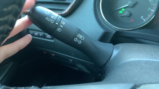 hand activating turn signal switch close-up shot on steering column with lever clicking, driving scene showing indicator control and vehicle signaling during road movement in car interior