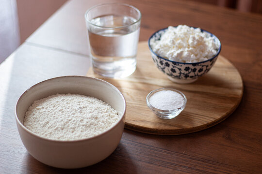 Baking ingredients on wooden table: flour, cottage cheese, water and sugar, rustic cooking setup