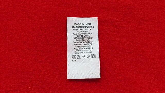 Closeup of made in india word and cotton clothing washing care instructions symbols tag label on cloth or fabric isolated on red table. Indian garments and textile manufacturing industry concept.
