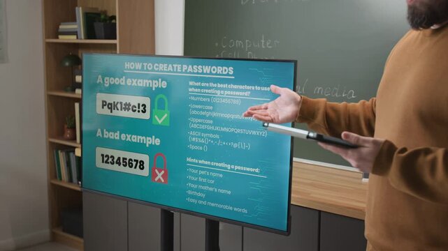 Side view close up shot of unrecognizable male teacher holding tablet in hands and talking in computer literacy class standing by digital board showing safe password examples in background, copy space