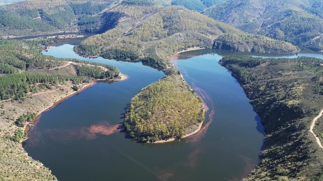 An S-shaped peninsula extends into calm waters, surrounded by a mountainous landscape. Ideal for environmental and travel content.