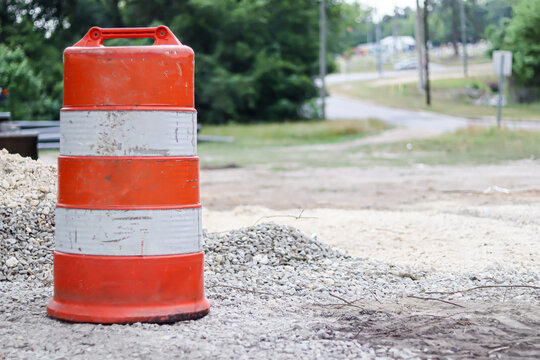 Orange construction traffic barrel on gravel road with heavy equipment in background