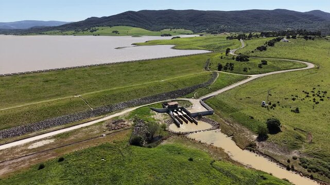 A tracking drone shot revealing the water release infrastructure at the base of the Barbate dam, surrounded by the green hills of Andalusia.