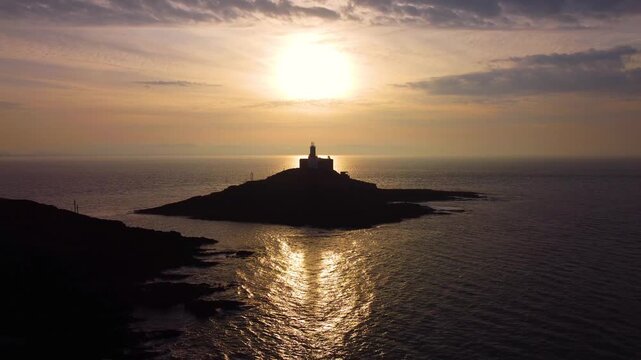 Descending Aerial of Mumbles Lighthouse at Sunrise with Shadow Cast on Sea. Golden Reflection of Sun on Ocean with Dynamic Clouds. Perfect for tourism, travel documentaries. Wales, UK. 4K.