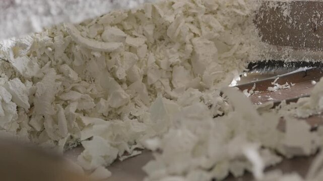 Large pile of shredded white polystyrene foam flakes and particles collected in recycling facility