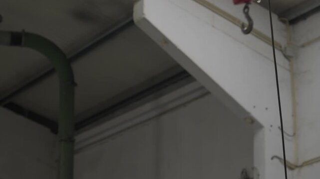Metal hook swinging back and forth over empty flat conveyor belt inside plastic recycling factory
