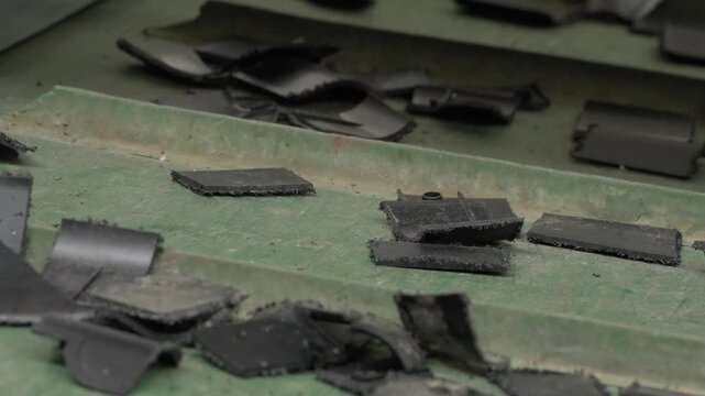 Large shredded black plastic chunks and fragments spread across green conveyor belt in recycling facility