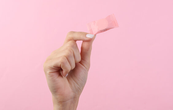 Woman's hand holding package of candy on pink background. Mockup for design.