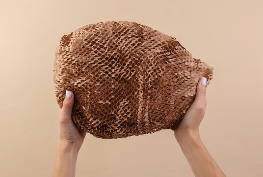 Female hands holding cardboard kraft honeycomb packaging shockproof for shipping on a beige background