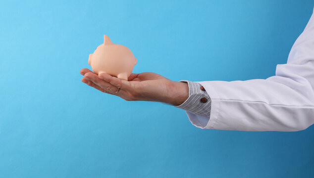 Doctor in a white medical coat holding piggy bank on a blue background