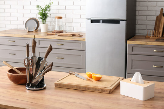 Wooden cutting board with orange and set of knives on table in kitchen