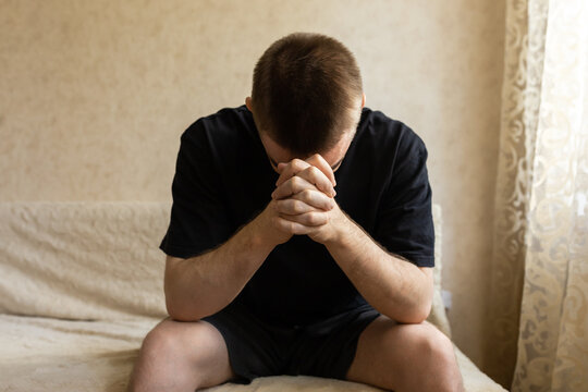 Thoughtful young man with clasped hands in close up indoors